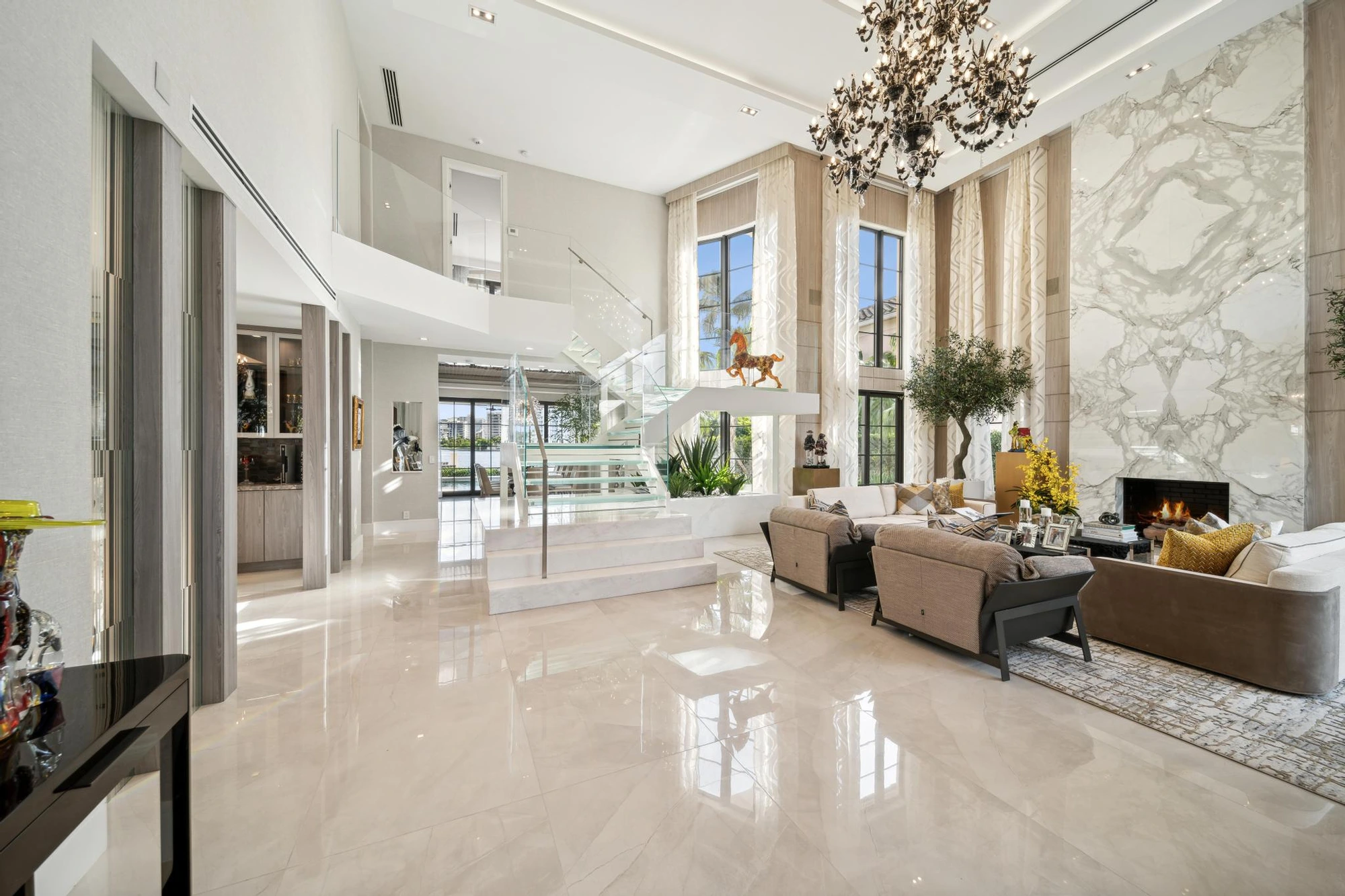 Double-height living space with a glass staircase and tall stone fireplace wall